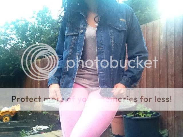 A person wearing a denim jacket and pink leggings.